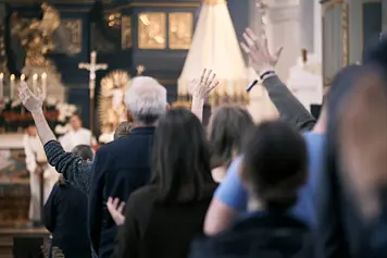 Easter monday celebration at Osterforum 2025. People in a church interior, some with arms raised, others with hands clasped in prayer.