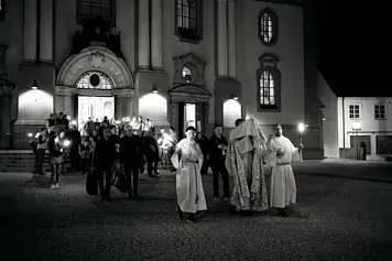 
                                        Maundy Thursday procession at Osterforum 2025: clergy in albs carry Sacrament, servers with torches, candlelit crowd before Saint Anna Cathedral.